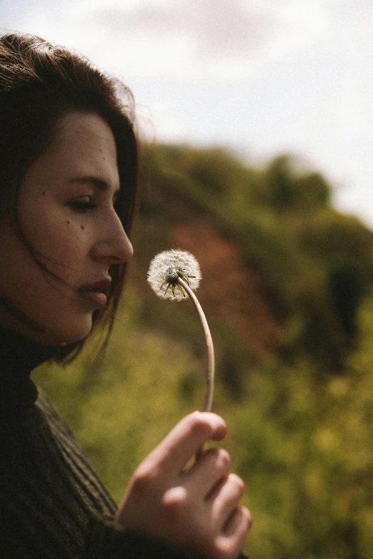 a woman is blowing a dandelion in her hand