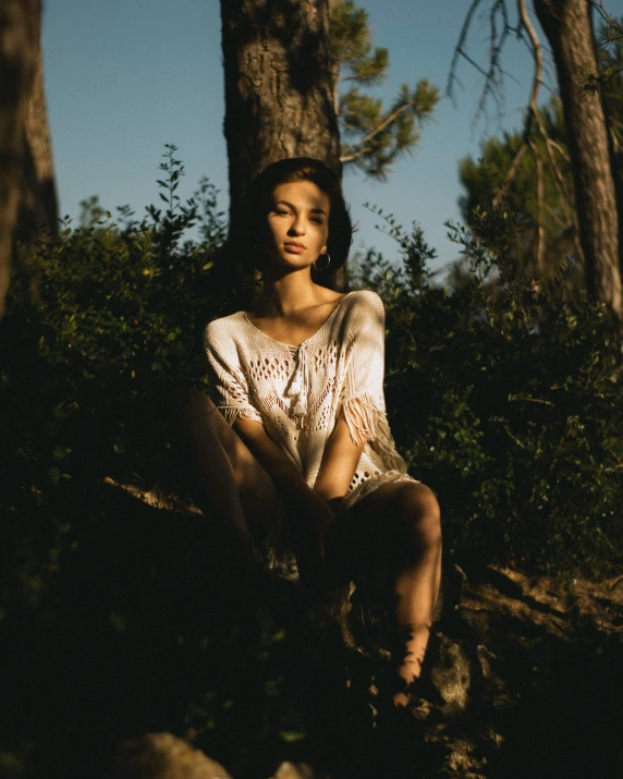 woman in a white dress sitting outside near trees