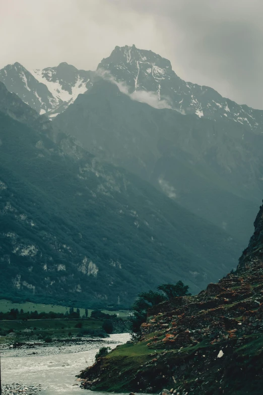 a mountain side with mountains in the background and a river running through it