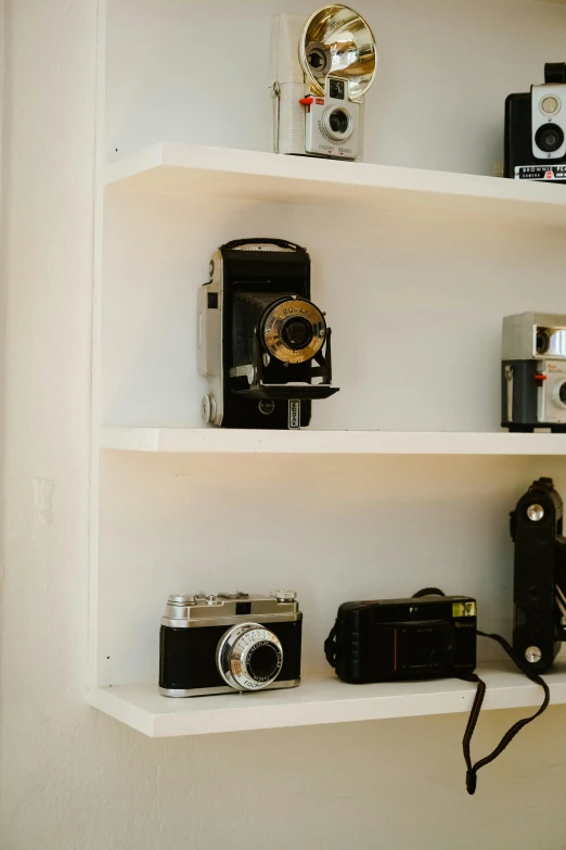 several antique cameras are sitting on two shelfs