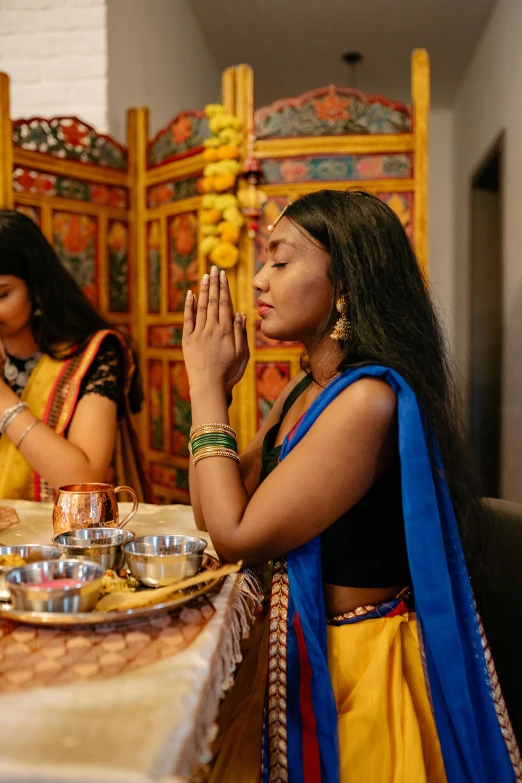 women in indian garb sitting at a table together, with food and plates