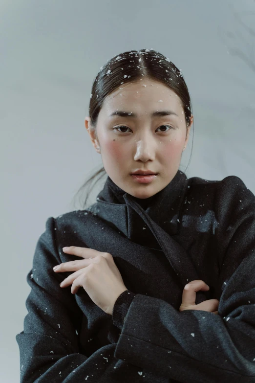an asian woman in winter wear with snow falling on her coat