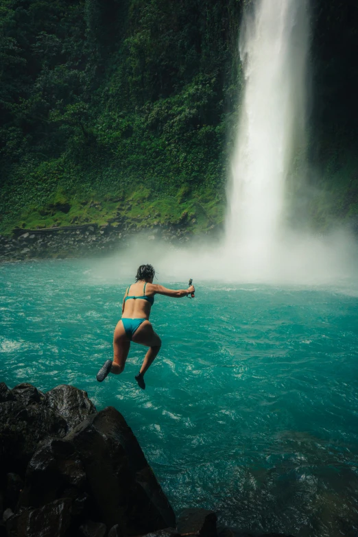 a woman in a bikini is jumping into the water near a waterfall