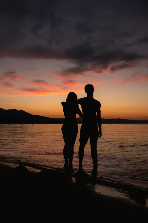 two people standing on a beach under a cloudy sky