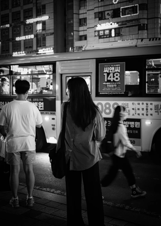 two people wait on the street next to a bus at night