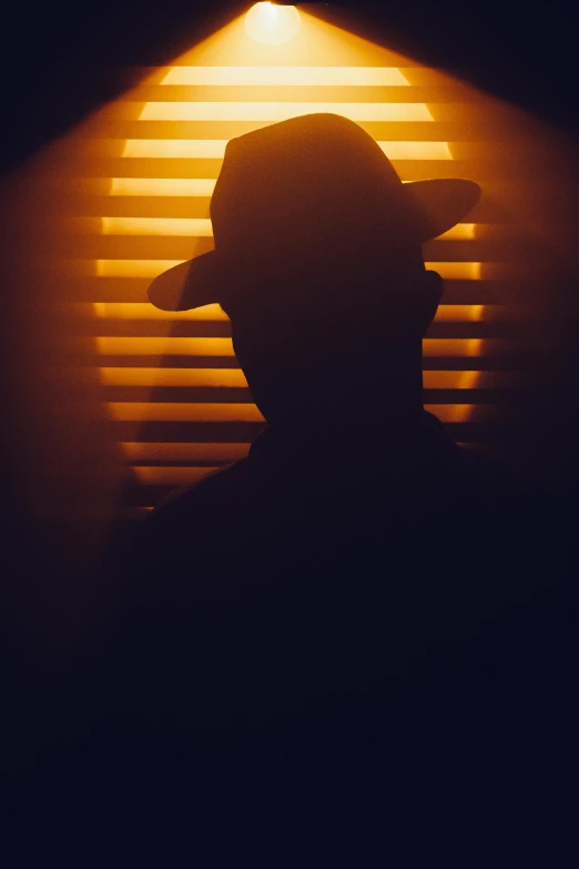 a person wearing a hat standing in front of a wall with a window light