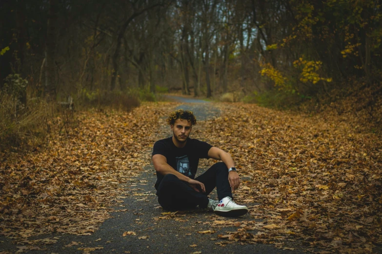 a man sitting on the floor in the middle of a leaf covered road