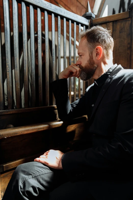 a man with a beard wearing a suit sitting on a bench