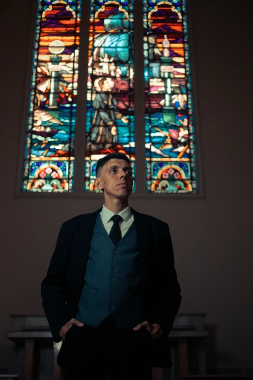a man wearing a suit and tie standing in front of a stained glass window