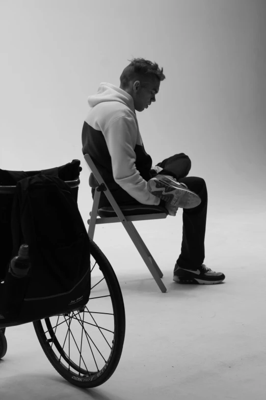 a man in a white hoodie sits on a folding chair next to a baby buggy