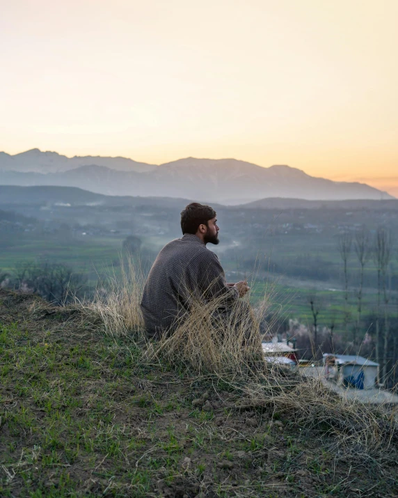 a man sitting on top of a grass covered hill