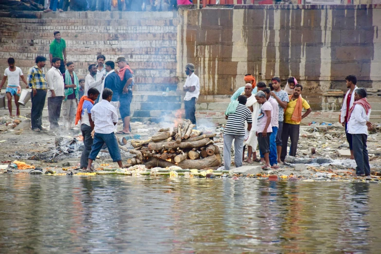 a group of people are standing in the water by a pile of wood