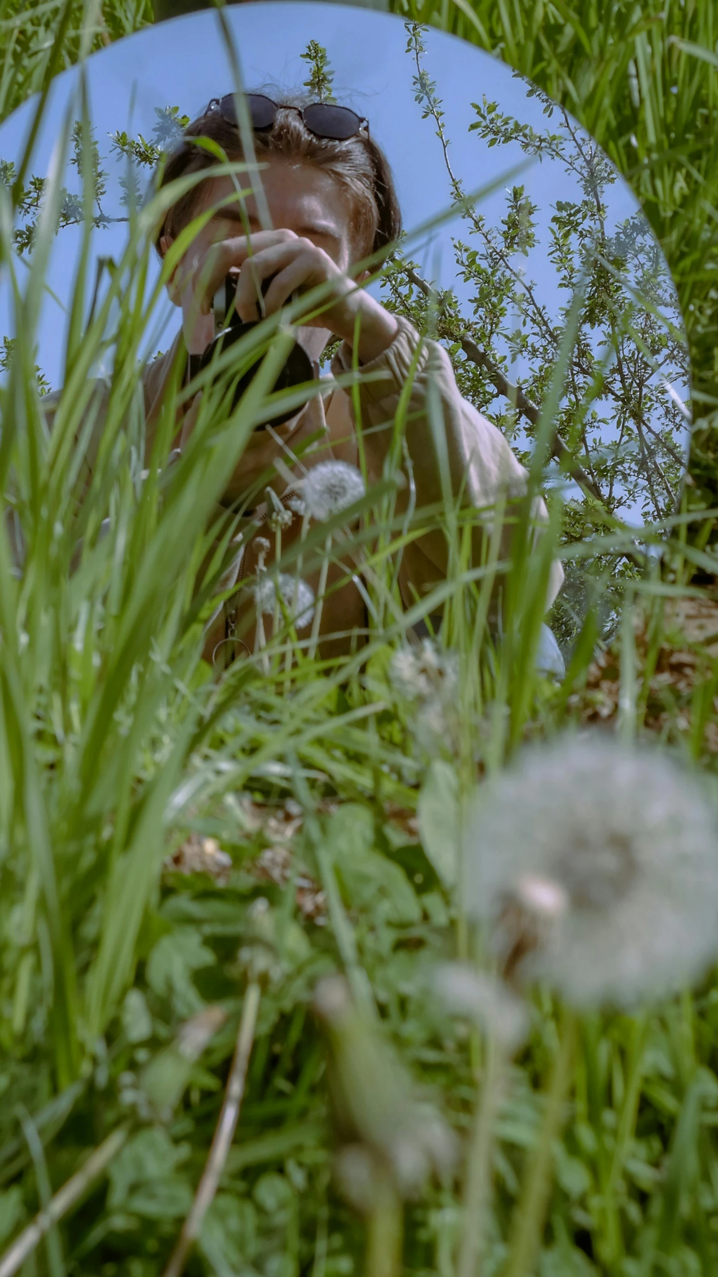 a girl in the grass taking a picture in a mirror