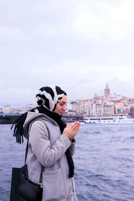 a woman standing on the side of the water holding her hands together