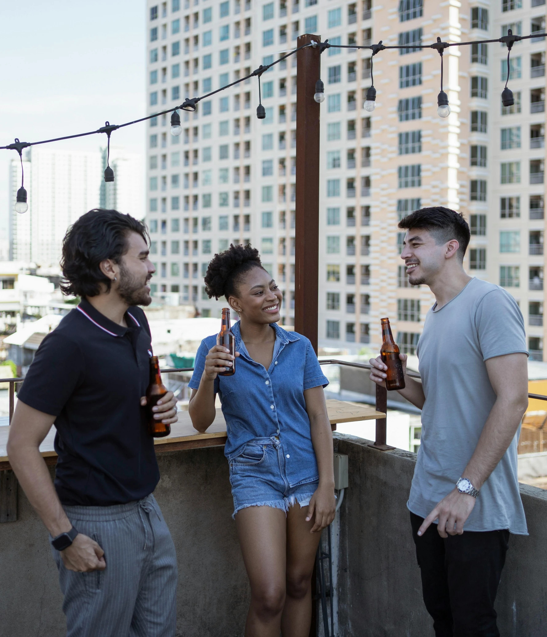 three friends laughing and drinking on a rooftop