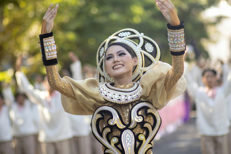 a woman dressed in white with a gold and black outfit is holding up her hands