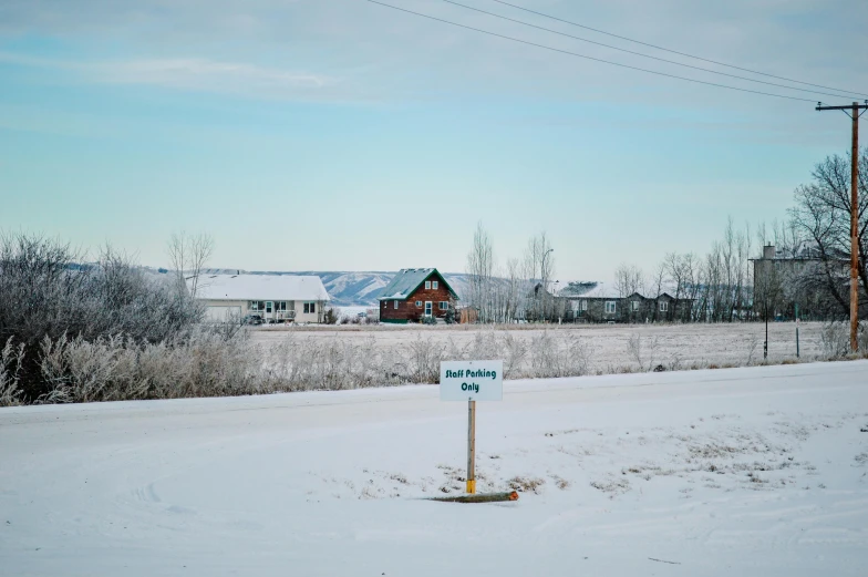 a street sign sits in the snow beside a rural house