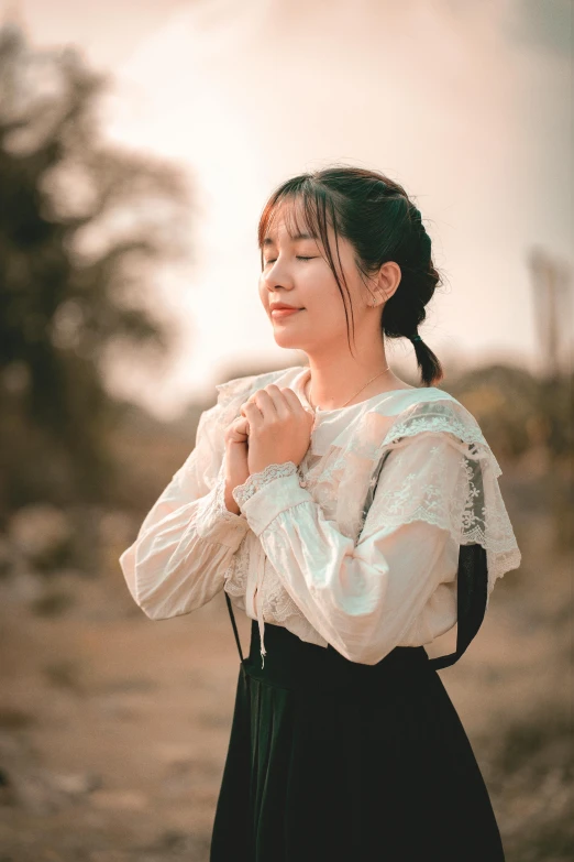 woman in white shirt and black skirt standing outdoors with her hands folded