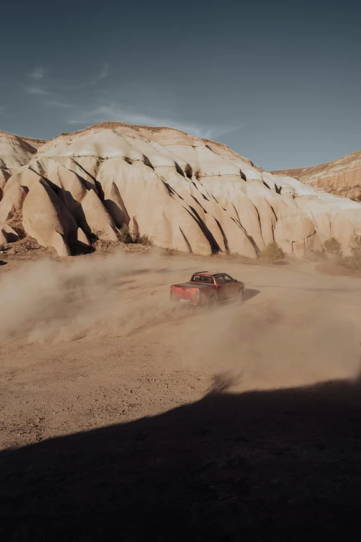 a truck rides down a hill as a dust trail approaches