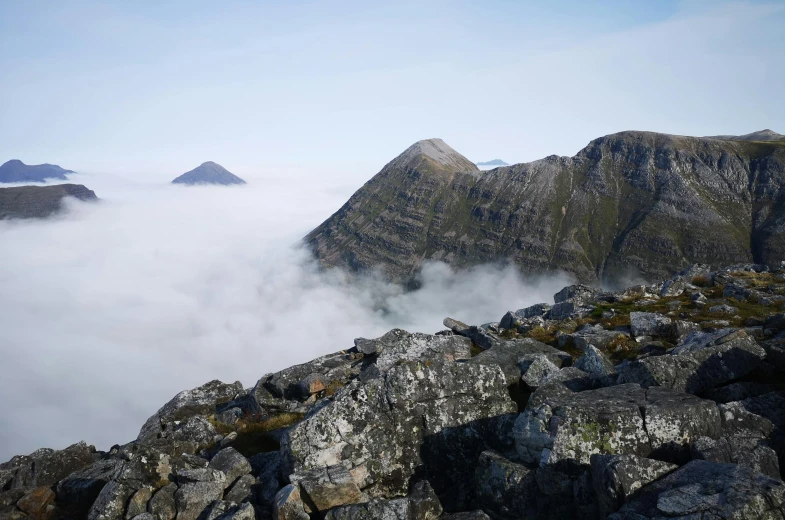 a mountain top with rocky layers and low clouds below