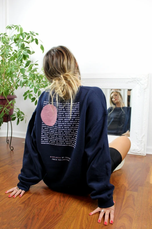 woman looking into mirror sitting on floor wearing sweatshirt