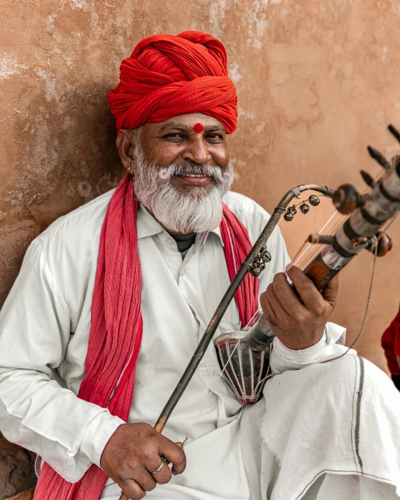 an old man with a red turban and a red scarf holding a small instrument