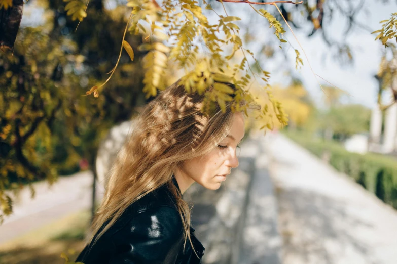 a young woman standing beneath trees, behind the nches is an image of a rock