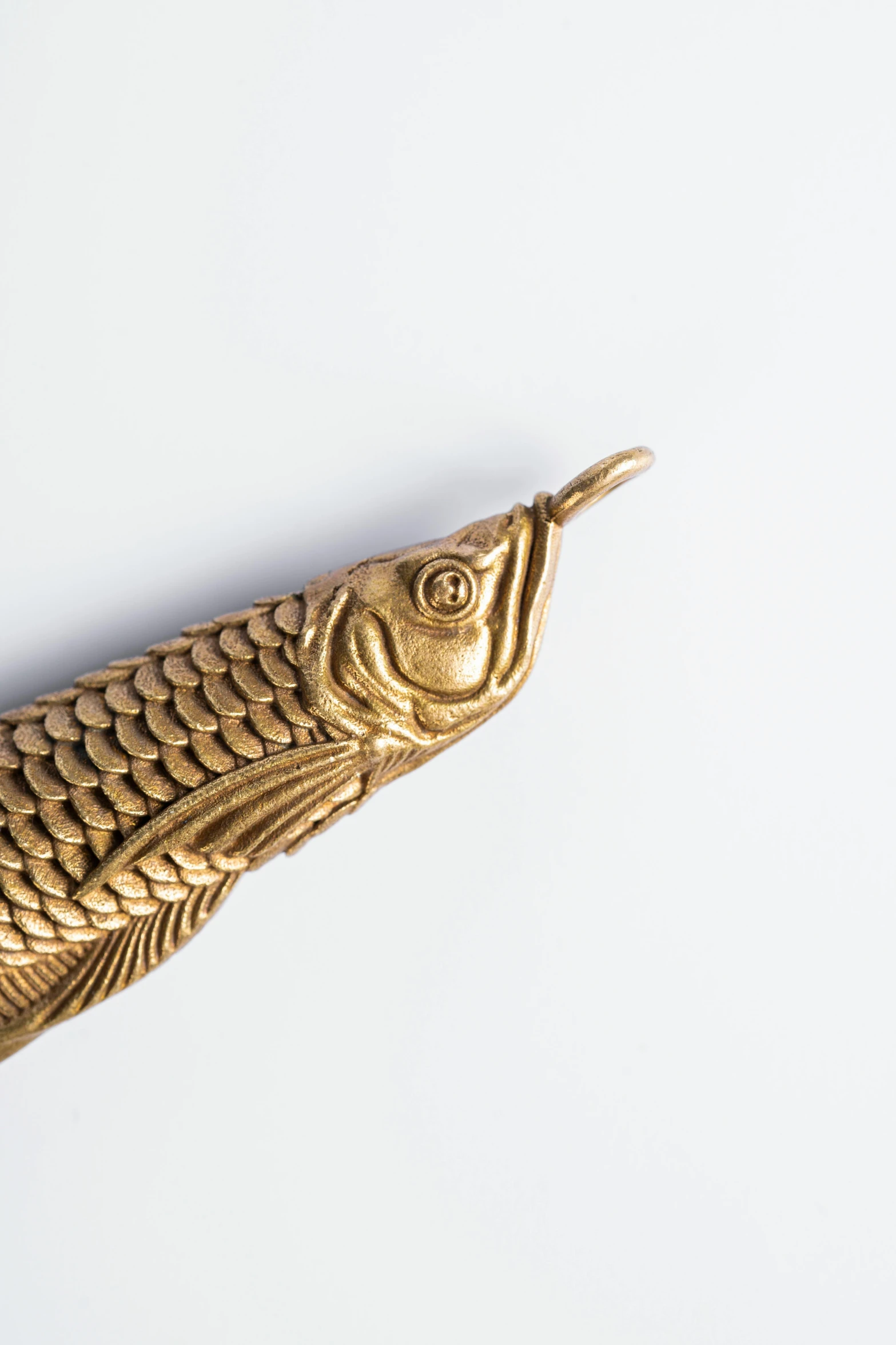 an ornate gold - toned metal fish on a white background