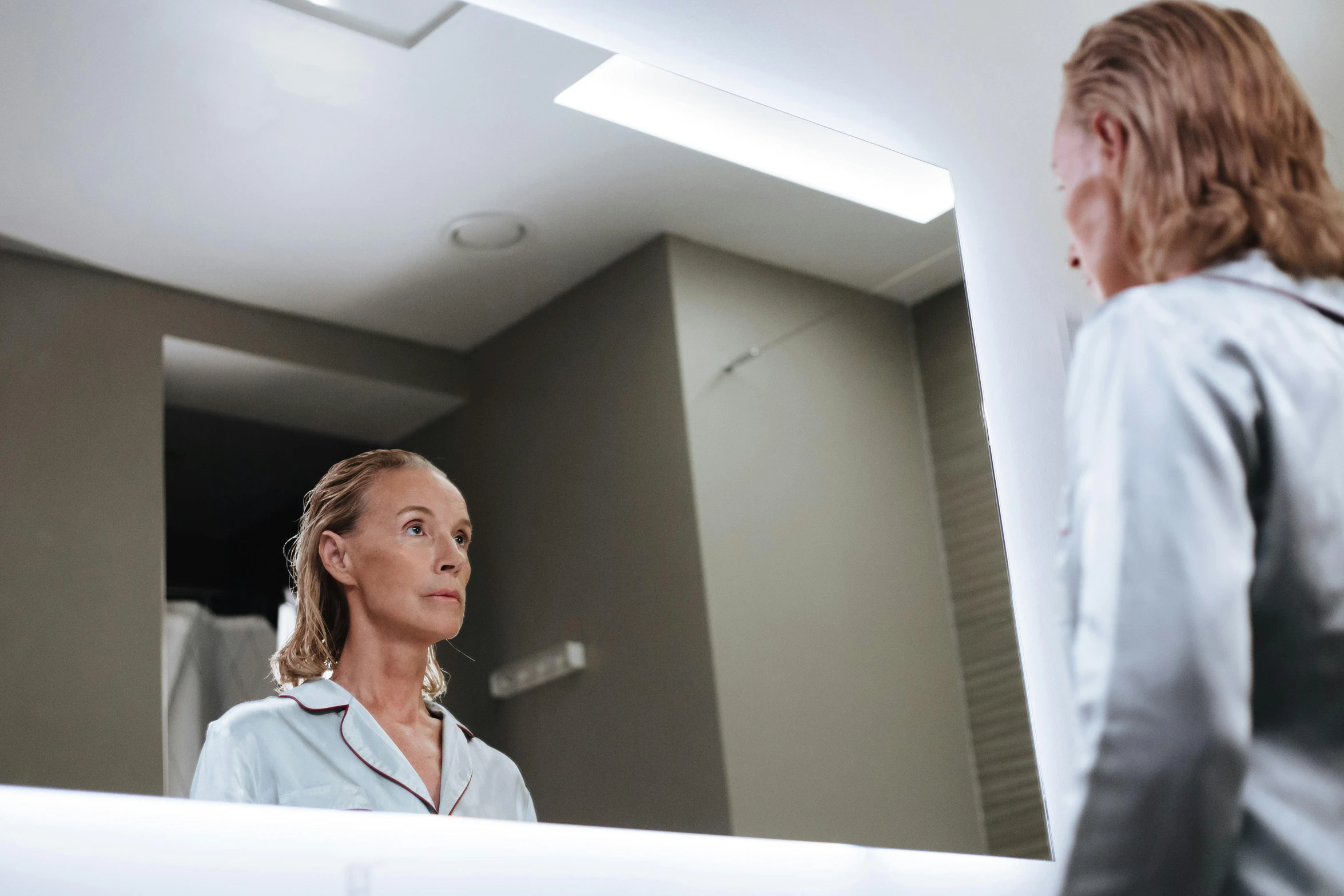 woman looking at reflection in bathroom mirror