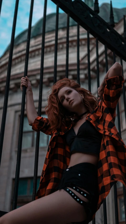 a young lady posing near a gate wearing short shorts and a plaid shirt