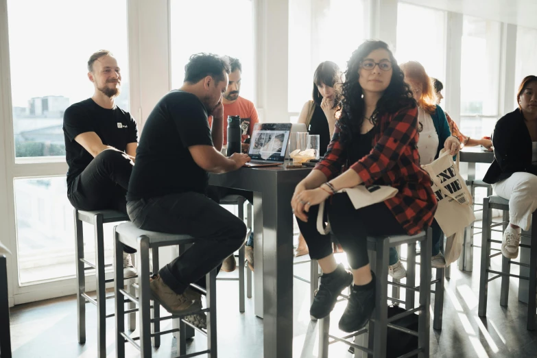 people sit around tables in a room that has multiple windows