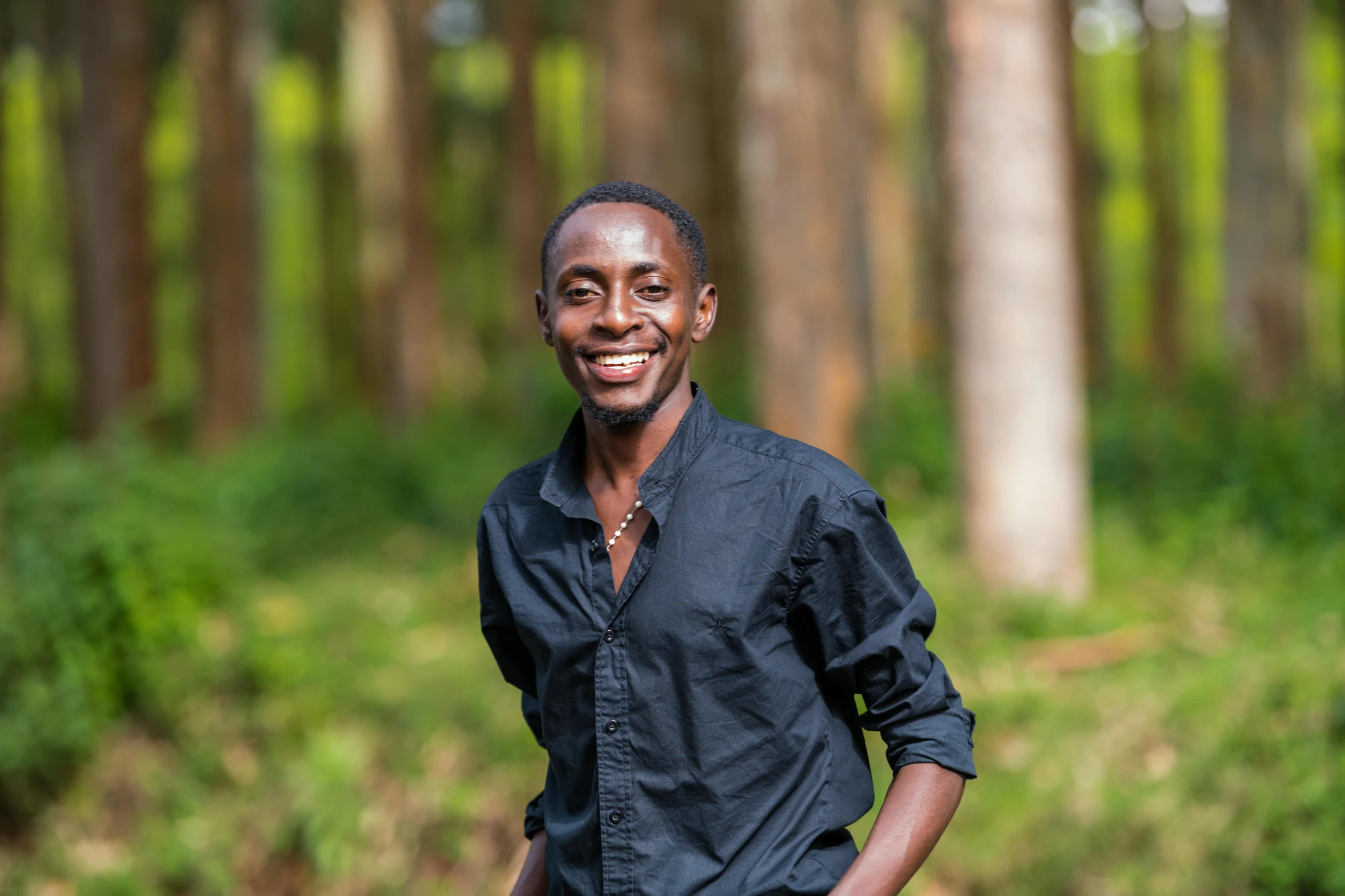 a man with a black shirt and tie standing in front of some trees