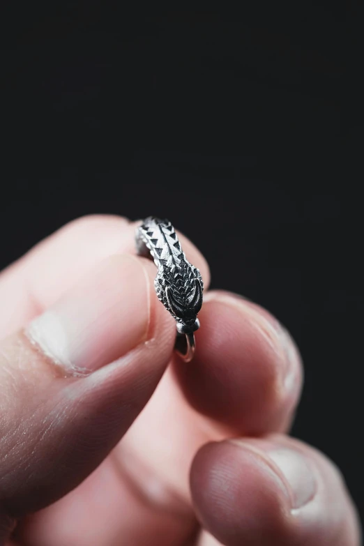 a finger holding a ring with a feather design on it