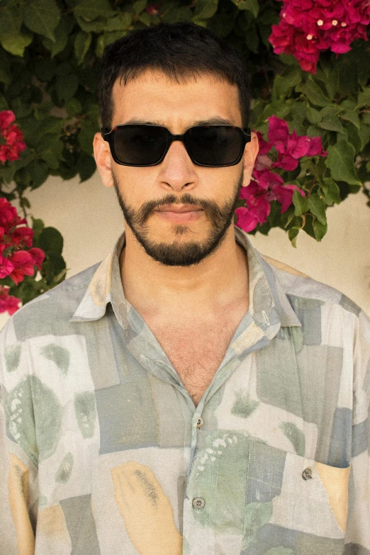 a man wearing shades stands in front of some pink flowers