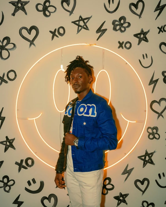 a man stands in front of a large white wall with neon writing