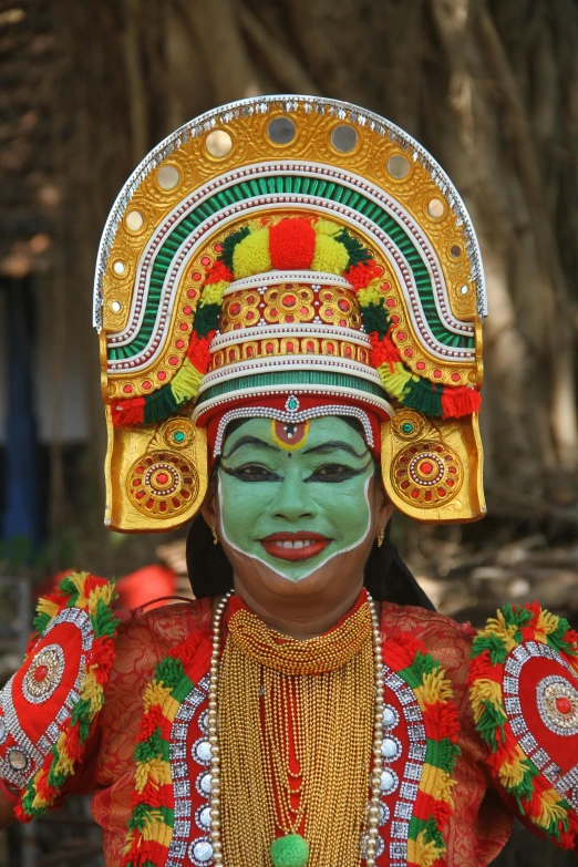 a man in mask, painted green with yellow accents and gold chains