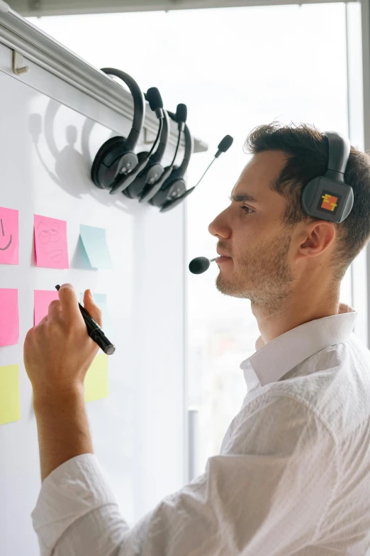 a man wearing ear phones is doing a post it with a white board