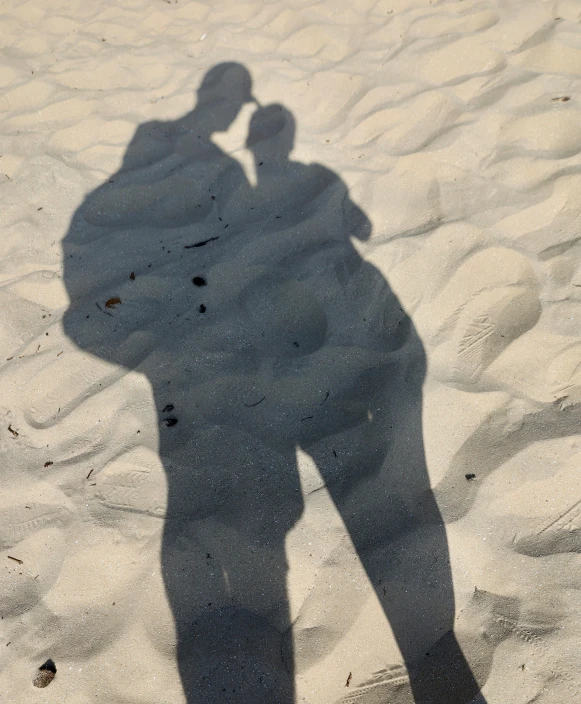 a shadow of two people standing in sand