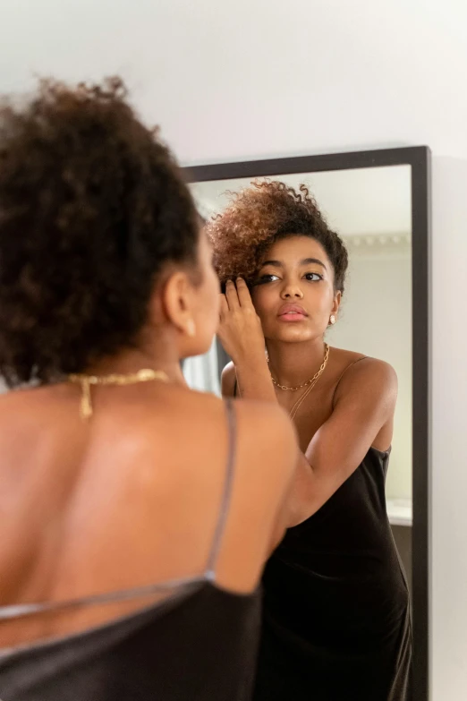 a woman in a dark dress combs her hair in front of a mirror