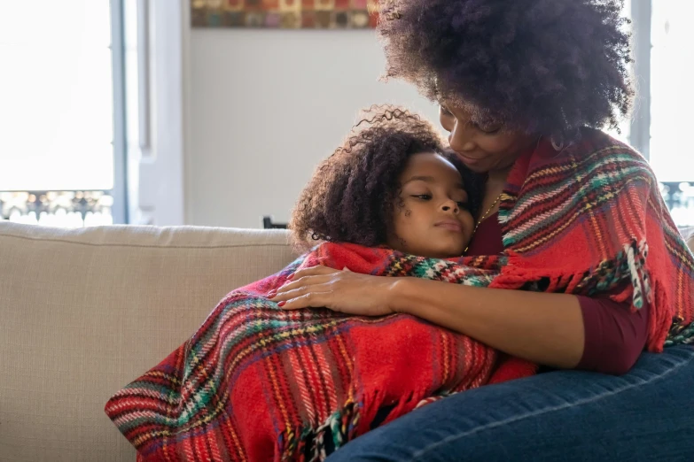 an adult and child wrapped in blankets hugging on a couch