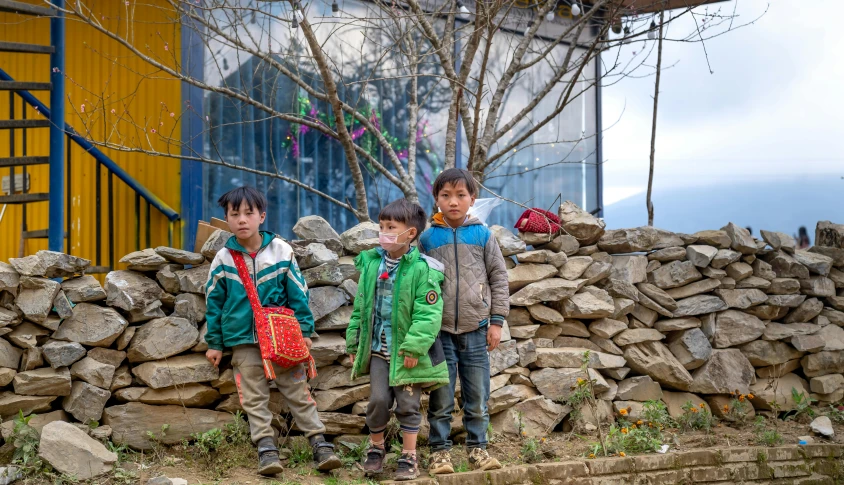 three small boys standing next to a pile of rocks