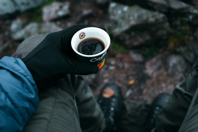 a cup of  drink being held by two pairs of black gloved hands