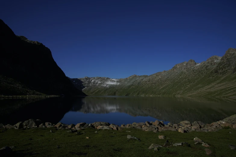 a small lake with rocks in the grass and mountains