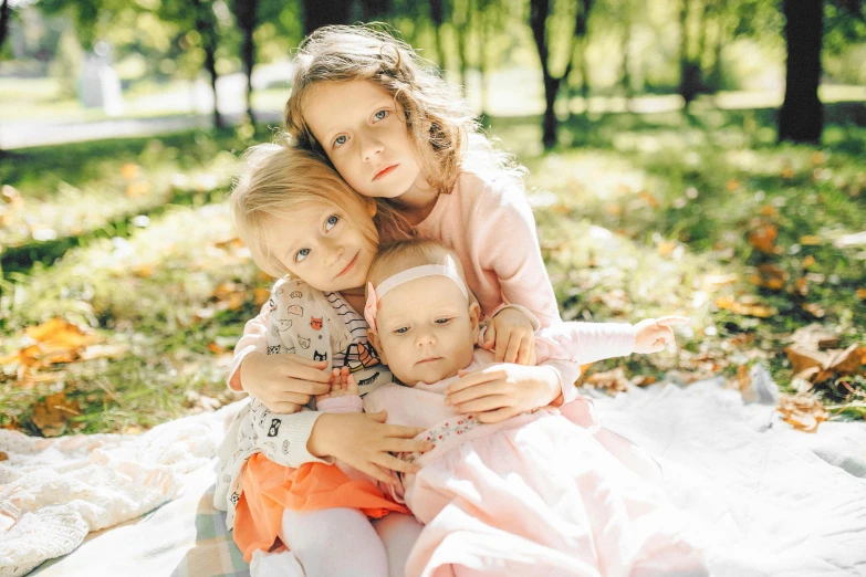 two little girls and a baby girl are sitting on a blanket in the leaves