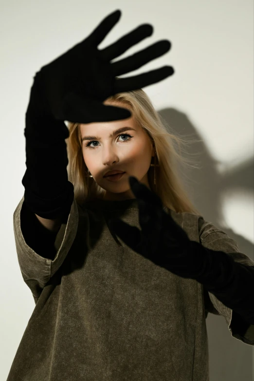 a woman in an olive sweater and black gloves holding her hand out