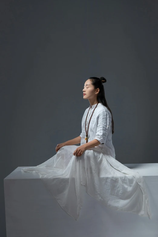 an asian woman sitting on a white ledge with her legs crossed