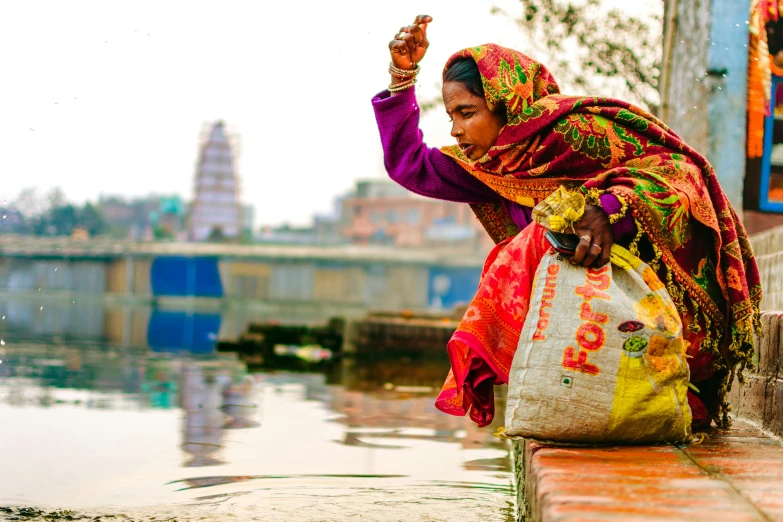 woman with colorful shawl squating in front of the water