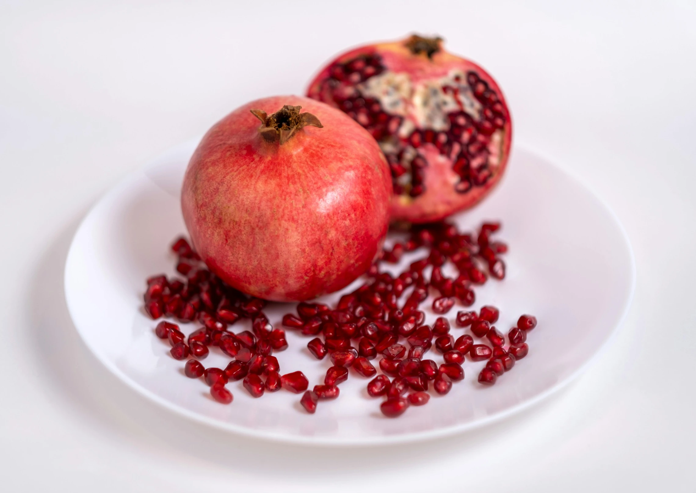 two pomegranates and one section of the whole pomegranate on a plate