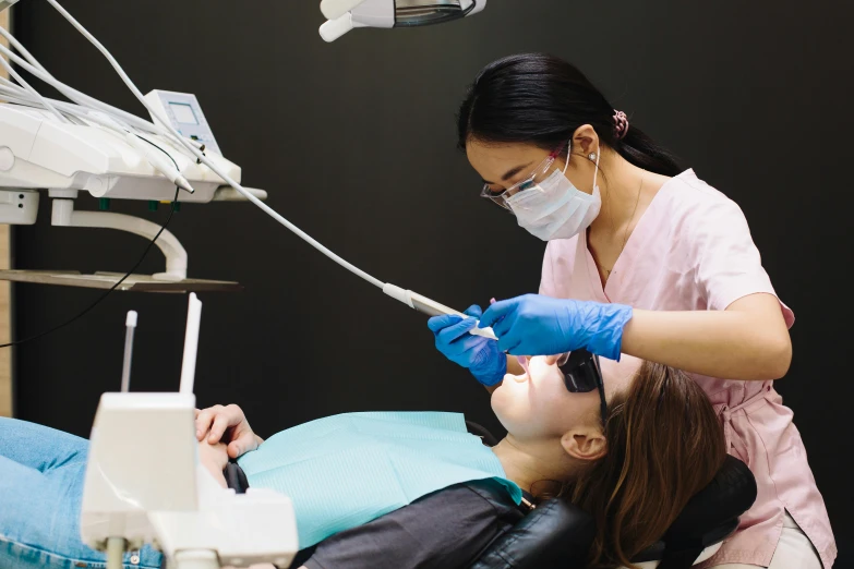 an asian woman getting her teeth brushed by a dentist