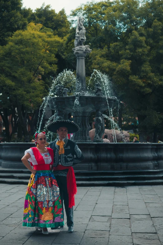 a man and woman in fancy clothing are standing next to a water fountain